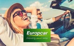 Dentro de um carro descapotável, uma mulher sorridente, usando camisa, chapéu e óculos de sol, tem as mãos atrás da cabeça. À sua esquerda, um homem jovem e sorridente, usando camisa e calças de ganga, conduz o carro. Em baixo, em destaque, o logótipo da rent a car Europcar, com a inscrição "moving your way".