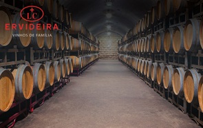 Plano cortado onde são visíveis vários barris de madeira usados para o estágio de vinhos, deitados, alinhados e organizados em diversos níveis. Em cima, à esquerda, o logótipo da marca de vinhos Ervideira, contendo por baixo a inscrição "Winemakers since 1880".