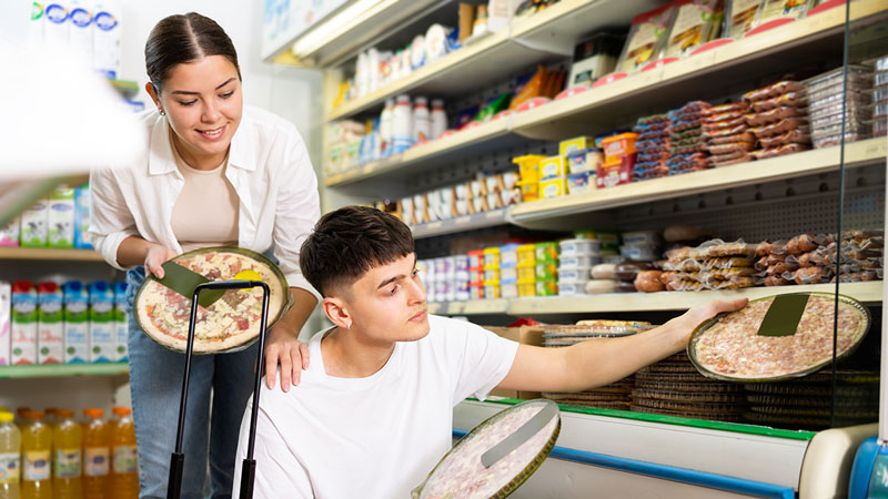 Casal jovem a escolher pizas frescas num expositor de supermercado 