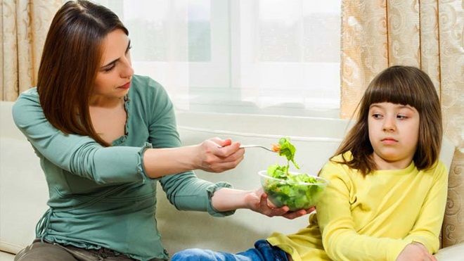 Mãe oferece salada a criança com ar enjoado