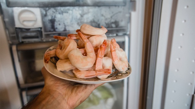 Pessoa a colocar prato com camarões congelados no frigorífico