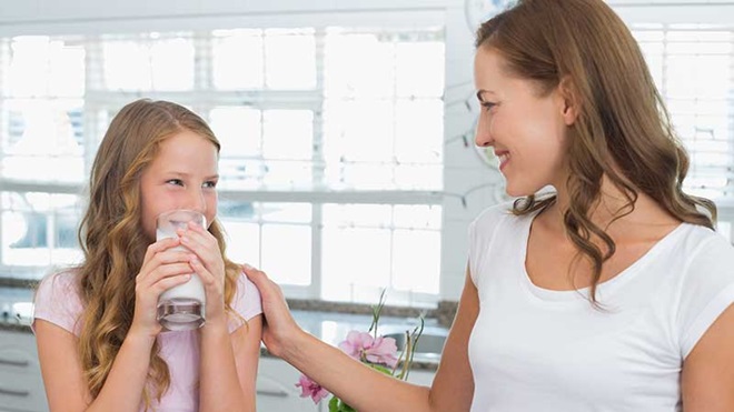 Mãe a ver a  filha a beber um copo de leite