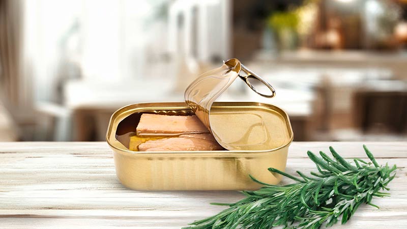 lata de atum em conserva em primeiro plano sobre uma mesa de madeira, numa cozinha