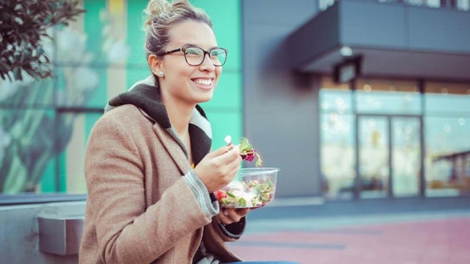 Rapariga a comer uma salada na rua