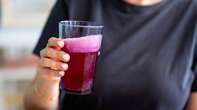 Pessoa com t-shirt azul escura a beber kombucha de frutos vermelhos