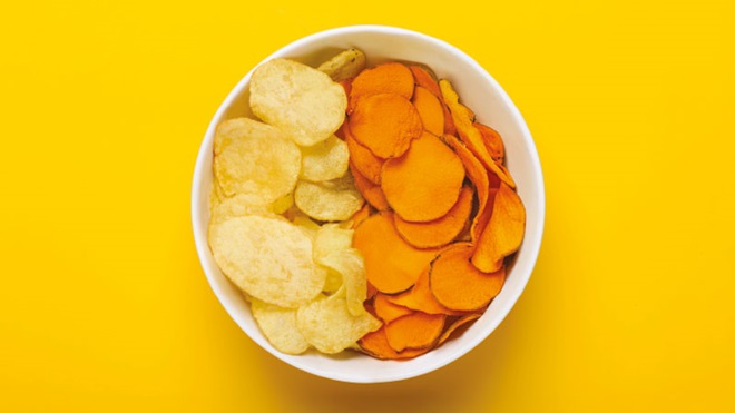 Grande plano de uma taça de batatas-fritas normais e de batata-frita doce, dentro de uma taça branca, com fundo amarelo