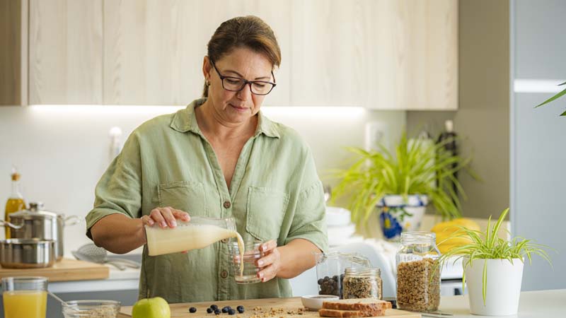 Mulher numa bancada de cozinha, a servir-se de bebida vegetal