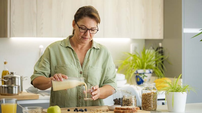 Mulher numa bancada de cozinha, a servir-se de bebida vegetal