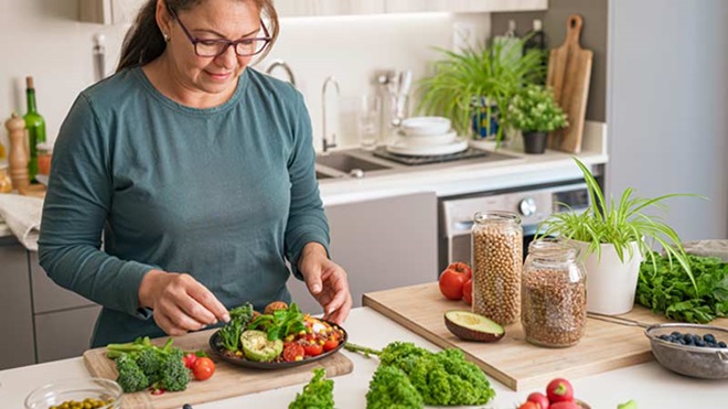 Mulher na bancada da cozinha a preparar refeição com alimentos saudáveis