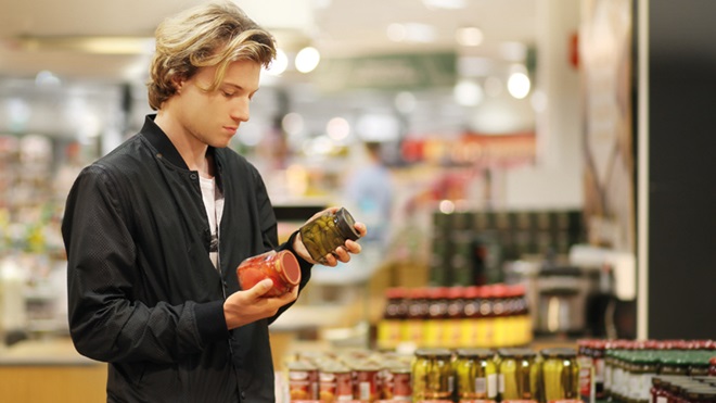 Homem num supermercado analisa a rótulos de frascos para procurar produtos sem glúten