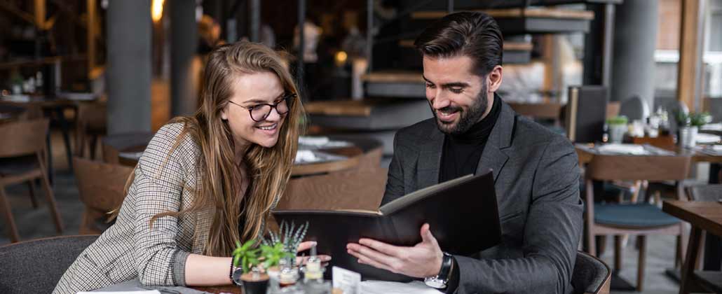 Casal num restaurante elegante decide o que quer pedir olhando para o menu