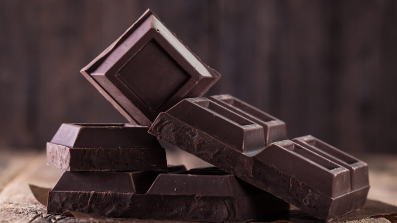 Pedaços de chocolare preto empilhados em cima de uma mesa de madeira