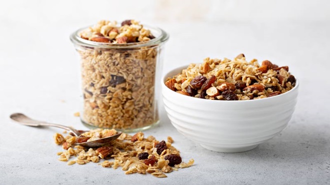 taça de vidro e taça de loiça com granola em cima de uma mesa, com uma colher ao lado