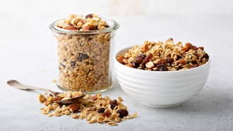 taça de vidro e taça de loiça com granola em cima de uma mesa, com uma colher ao lado