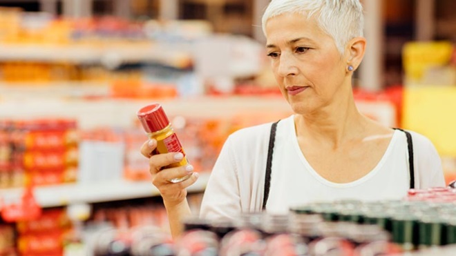 Mulher a fazer compras num supermercado, com o olhar focado no rótulo de uma embalagem alimentar