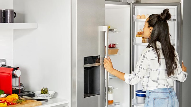 Mulher jovem olha para dentro do frigorífico, na sua cozinha