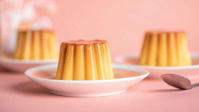 3 pudins de ovos em pires, sobre uma mesa com uma colher ao lado - alusão a pudins de ovos embalados