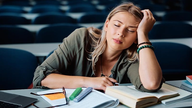 Estudante universitária cansada a estudar para exames numa sala de aula