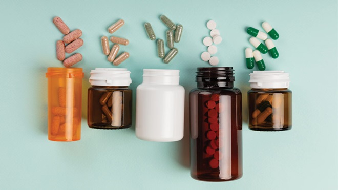 Frascos sobre um fundo verde, com suplementos em comprimidos e cápsulas de várias cores