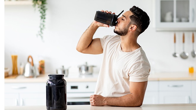 homem a beber uma bebida com proteína em pó, na cozinha