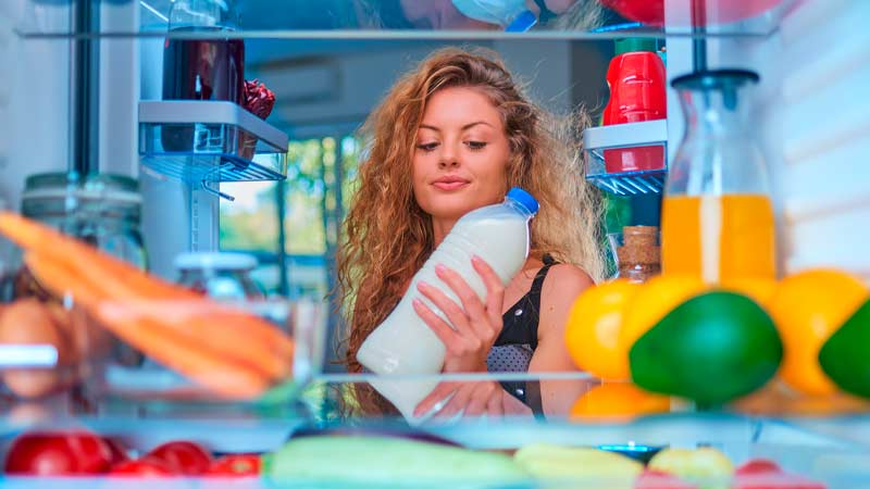 Mulher a olhar para o interior do frigorífico e a verificar a o prazo de validade de uma embalagem de leite 