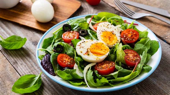 Prato de vegetais sobre uma mesa de madeira, com um ovo cortado ao meio por cima - alusão a ovolactovegetarianismo