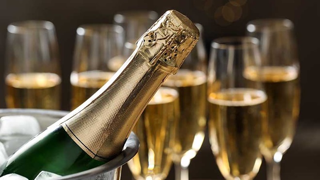 Garrafa de espumante dentro de balde de gelo, com flûtes em fundo