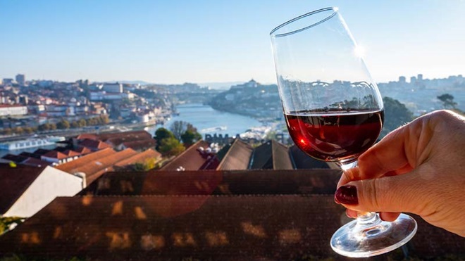 Grande plano de mão de mulher a segurar num cálice de vinho do Porto numa varanda com vista sobre o Douro