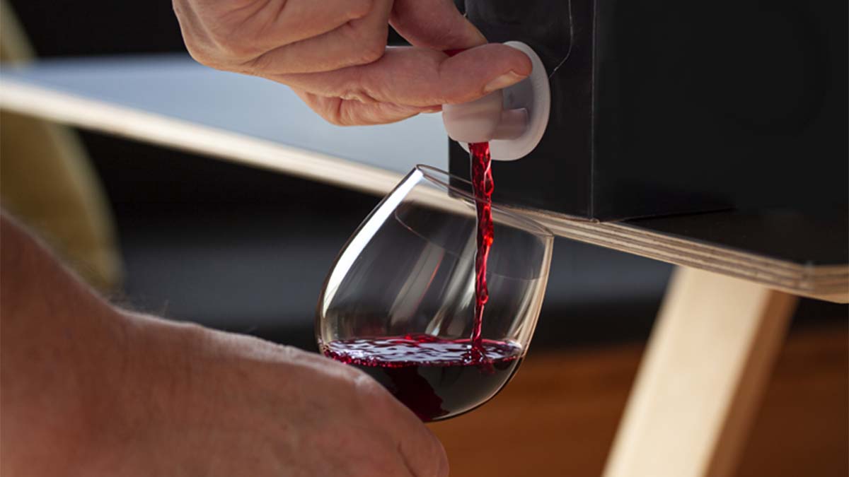 Grande plano de mão a encher um copo com vinho tinto a partir da torneira de bag in box 