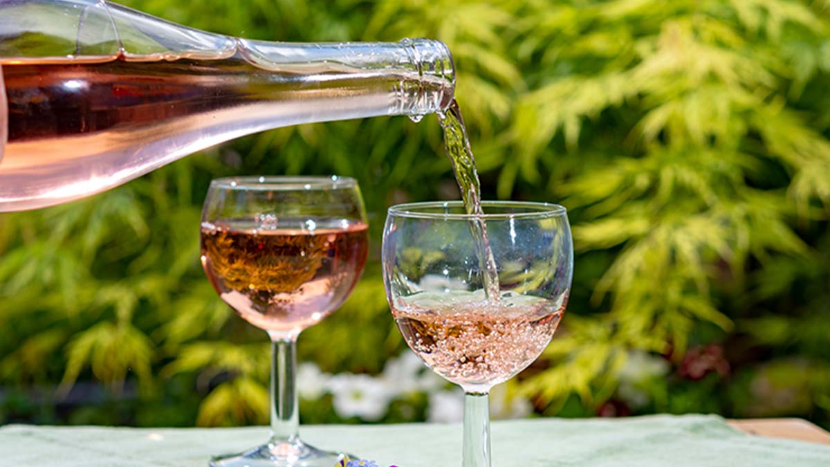 Vinho rosé a ser servido em dois copos no exterior, com paisagem de vinhas como pano de fundo 