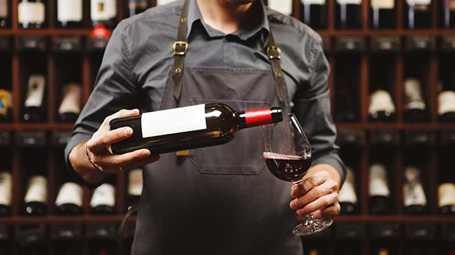 homem em garrafeira a deitar vinho para copo