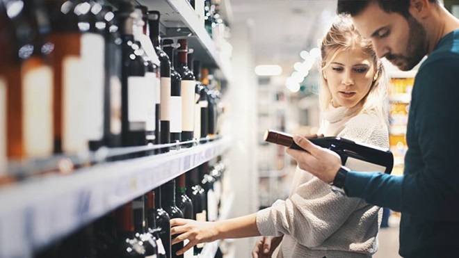 Casal no supermercado a escolher vinhos e a analisar rótulos