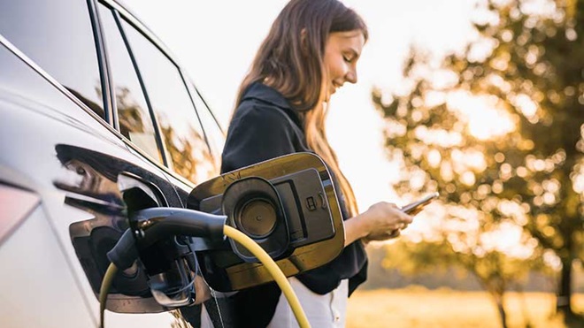 Mulher ao telemóvel a carregar o automóvel elétrico