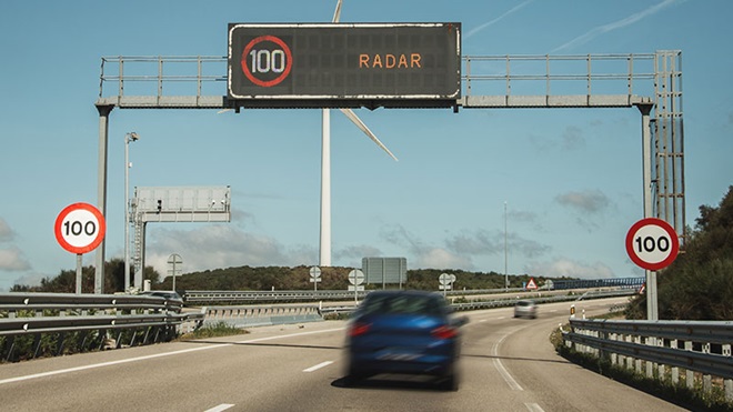 carro a passar por pórtico de autoestrada que mostra informação de radar e limite 100 de velocidade