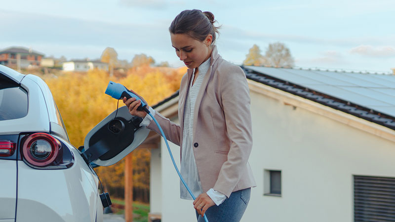 Mulher a carregar carro elétrico branco em casa