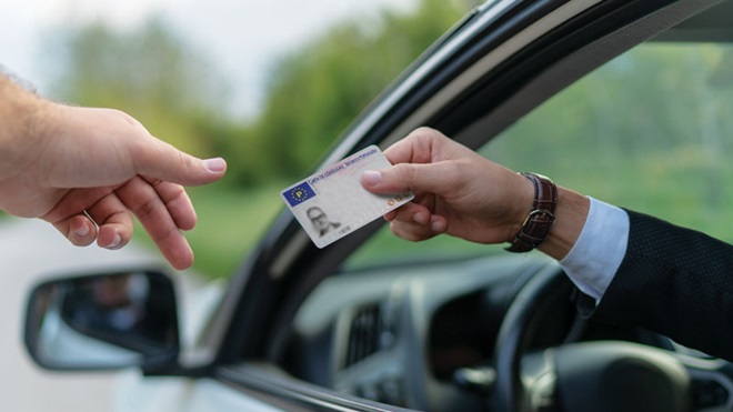 Pessoa dentro do carro mostra carta de condução (desfocada) a uma mão de agente de autoridade