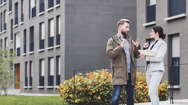 Homem e mulher conversam em frente a prédios de um condomínio