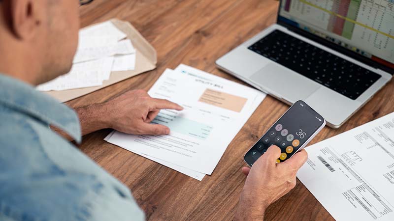 homem a fazer cálculos de faturas com smartphone e computador portátil