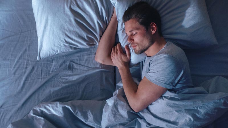 homem deitado de lado a dormir com duas almofadas