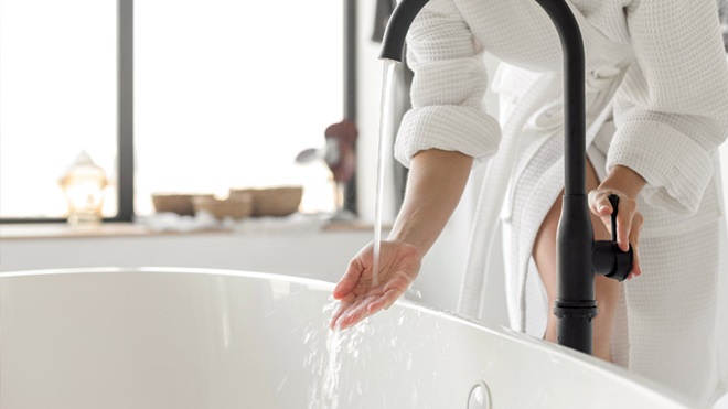 Mulher a molhar a mão na torneira da banheira