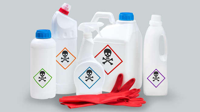 Várias embalagens brancas de detergentes com o símbolo de perigo no rótulo e duas luvas vermelhas à frente.