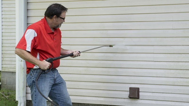 homem a limpar porta de uma garagem com máquina de limpeza de alta pressão