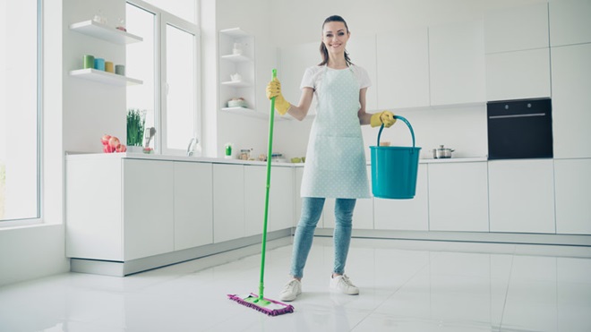 Mulher numa cozinha segura balde e esfregona para lavar o chão, ar feliz