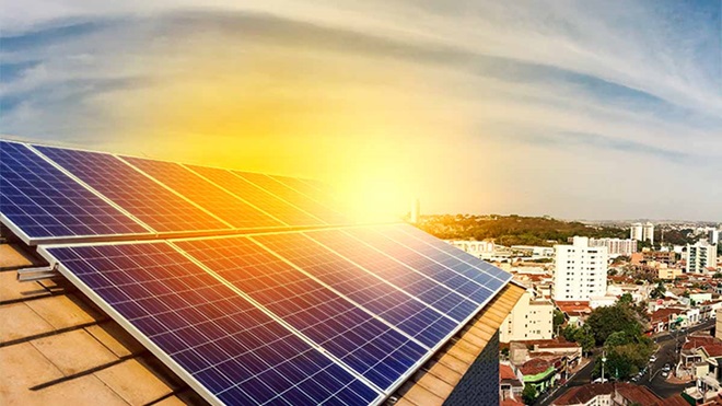 Painéis solares num telhado de uma casa. Sol ao fundo