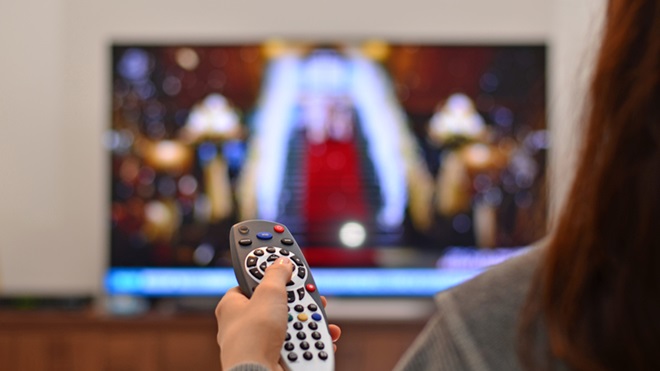 Mulher com um comando na mão em frente ao televisor