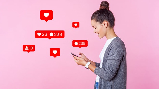 rapariga a usar telemóvel com vários ícones referentes a likes e comentários em redes sociais sobre um fundo rosa