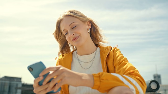 Jovem a segurar telemóvel, com ar descontraído, num terraço de um prédio