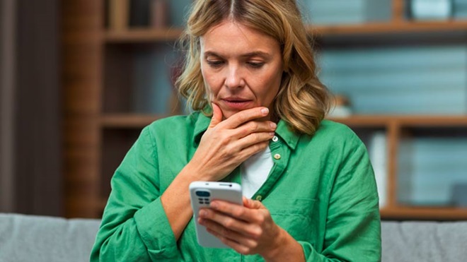 Mulher com ar preocupado olha para ecrã de telemóvel - alusão a burlas com chamadas internacionais