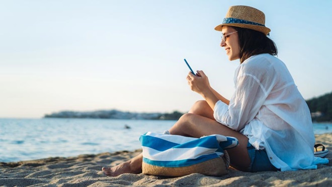 mulher na praia com telemóvel na mão