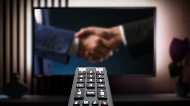 Televisão mostrando aperto de mão no ecrã, telecomando em primeiro plano